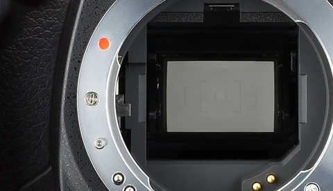 Interior view of a camera body with mirror removed, showing the sensor and mirror box assembly with black housing and light gray sensor surface.