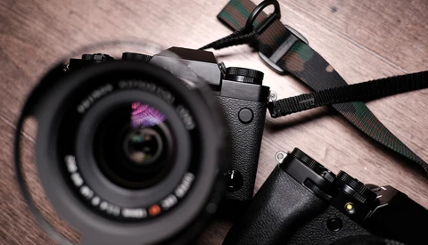 Mirrorless camera with zoom lens and camera strap on wooden surface.
