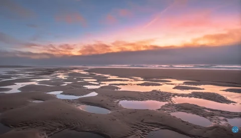 Aerial view of tidal flats and shallow pools at sunset with pink and orange sky.