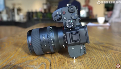 Mirrorless camera with attached prime lens mounted on wooden surface in indoor setting.