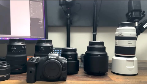 Canon DSLR camera body surrounded by various lenses on a wooden surface.