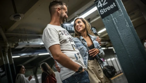 Couple standing in a subway station beneath a 42 Street sign, engaged in conversation.