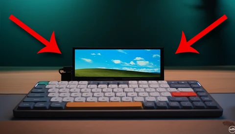 Illustration of a mechanical keyboard with a small monitor displaying a landscape scene, flanked by two red arrows pointing downward.