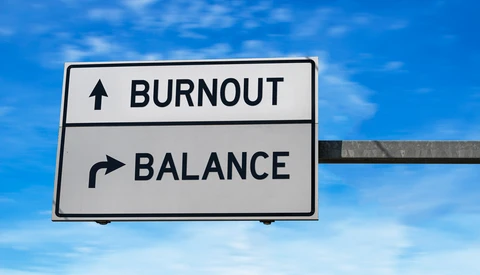 Road sign with two directional options: burnout pointing upward and balance pointing right, set against a blue sky.