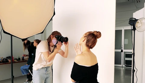 Photographer shooting a portrait of a woman against a white backdrop in a studio setting.