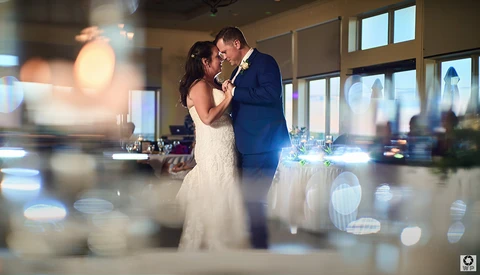 Bride and groom kissing during first dance with bokeh lights in foreground.