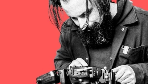 Photographer holding a film camera against a bright red background.