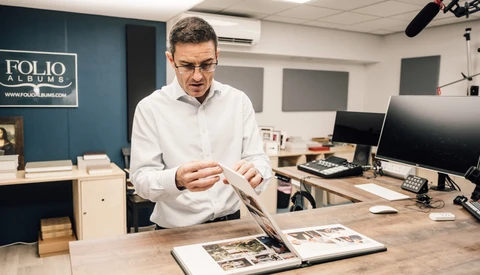 Man in white shirt examining open portfolio books at wooden desk in studio.