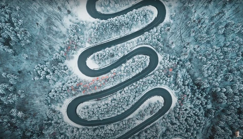 Aerial view of a winding mountain road cutting through snow-covered forest.