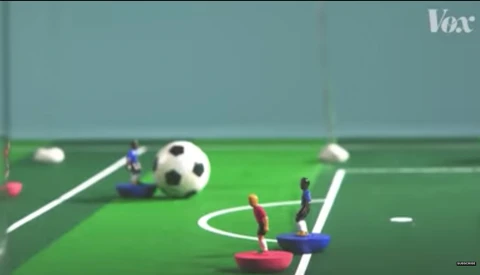Illustration of a miniature soccer field with figurine players and a ball.
