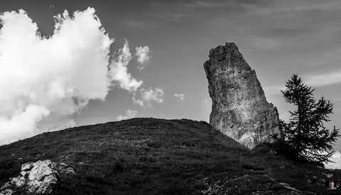 Dramatic rocky pinnacle rising from a forested hillside beneath cloudy sky.