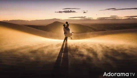 Silhouetted figure standing on desert sand dunes during golden hour sunset with dramatic atmospheric dust clouds.