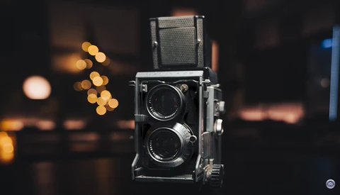 Vintage twin-lens reflex camera with folded viewfinder against blurred warm bokeh background.