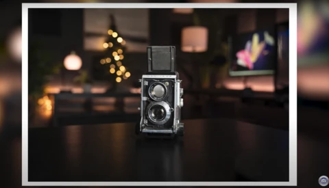 Vintage twin-lens reflex camera displayed on a dark surface with warm bokeh lights in the background.
