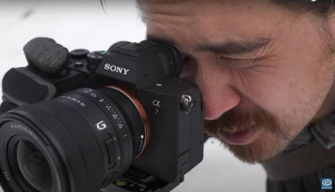 Photographer holding a Sony Alpha 7 mirrorless camera with an external microphone mounted on top.