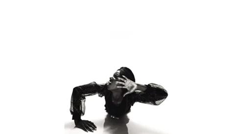 High-contrast black and white studio portrait of a shirtless man in a dramatic crouching pose against a white background.