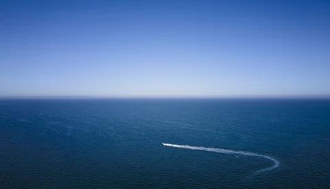 Aerial view of a speedboat leaving a curved wake across calm blue ocean water.