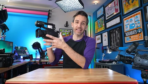 Content creator holding a compact video camera in a colorful studio setup with blue walls and professional lighting.