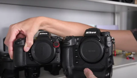 Hands holding two Nikon DSLR camera bodies side by side for comparison.