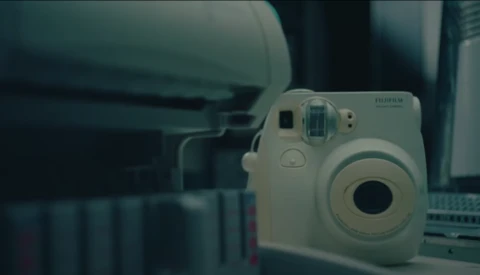 White Fujifilm Instax Mini instant camera displayed on a desk beside a laptop keyboard.
