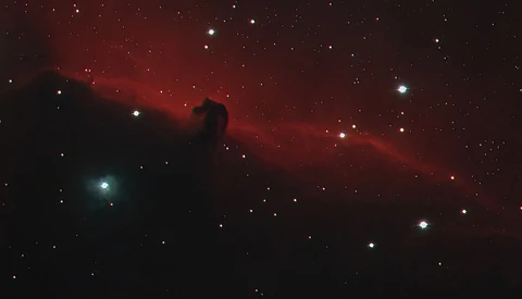 Deep-space photograph showing a dark nebula silhouetted against red hydrogen emission clouds and scattered stars.