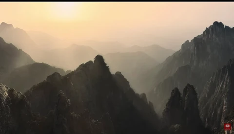 Misty mountain valley at sunrise with layered peaks silhouetted against golden light.