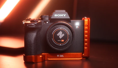 Sony mirrorless camera with red L-bracket mounted on dark surface under warm studio lighting.