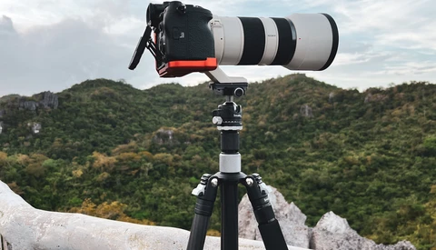 Telephoto lens mounted on tripod overlooking forested hillside with stone fortification.