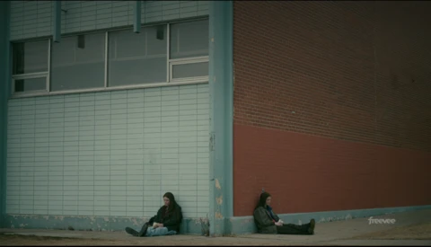 Two people sitting separately against a colorful urban wall with turquoise and rust tones.