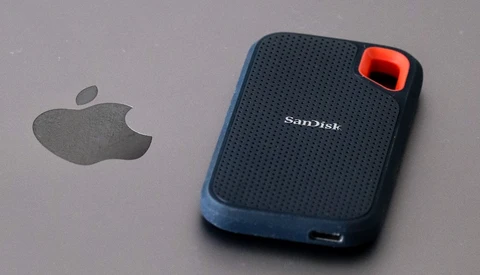 SanDisk Extreme portable solid-state drive with red button next to Apple logo on gray surface.