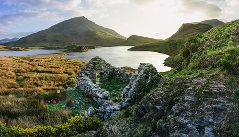 Glacial lake surrounded by moss-covered lava rock formations and green mountainous terrain under partly cloudy sky.