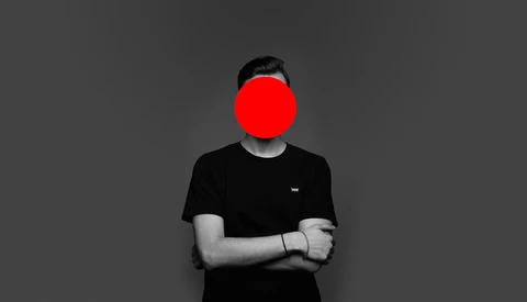 Person in black t-shirt with arms crossed, face obscured by large red circle.