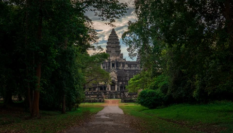 Ancient stone temple tower framed by tree-lined pathway in verdant garden setting.
