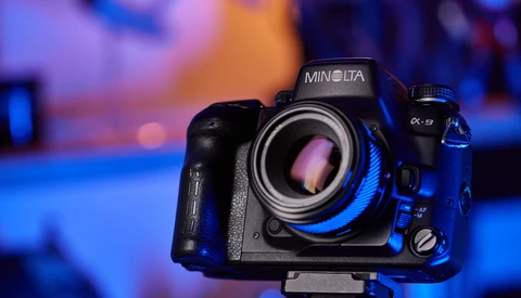 Minolta α-9 camera with blue accent lighting against a colorful bokeh background.