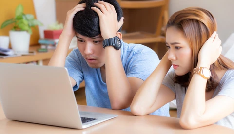 Two young people looking at a laptop screen together with concerned expressions in a home office setting.