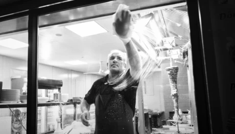 Man cleaning a large window from inside, reaching upward with a squeegee or cleaning tool.
