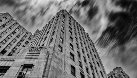 Upward view of tall Art Deco building with dramatic clouds and motion blur.