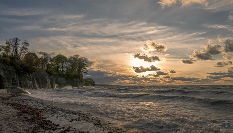 Dramatic coastal landscape with eroded cliff, beach, and golden sunset sky with storm clouds.