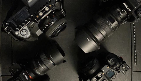 Professional camera gear layout including Nikon bodies, lenses with hoods, and accessories arranged on a dark surface.