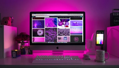 Mac monitor displaying a grid of magenta and purple-toned landscape and floral photographs in a color-graded workspace.