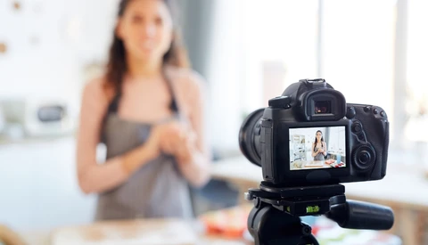 Professional DSLR camera on tripod displaying live video feed of a woman in an indoor kitchen setting.