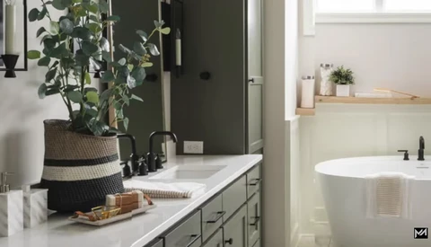 Modern bathroom vanity with marble countertop, potted plant, and freestanding soaking tub visible in background.