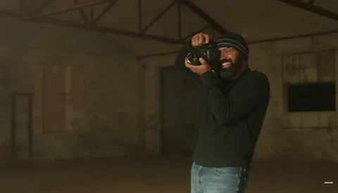 Photographer holding camera to eye while looking through viewfinder in an industrial warehouse space.