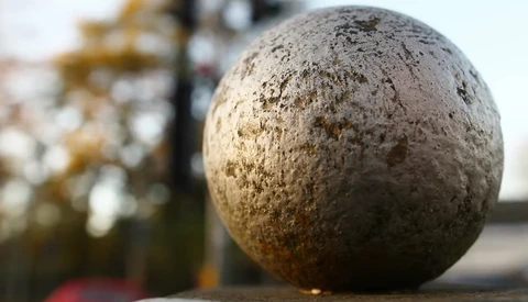 Close-up of a weathered concrete sphere with textured surface and golden-brown discoloration.