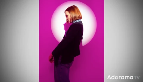 Woman in dark blazer photographed in profile against a bright circular magenta backdrop with soft halo lighting effect.
