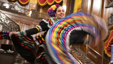 Performer in colorful striped costume spinning a rainbow hula hoop indoors.