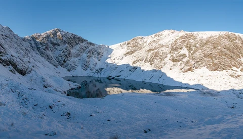 Snow-covered mountain valley with coniferous trees and peaks under clear blue sky.