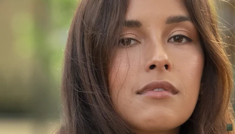Close-up portrait of a woman with long dark hair and a contemplative expression against a blurred green background.