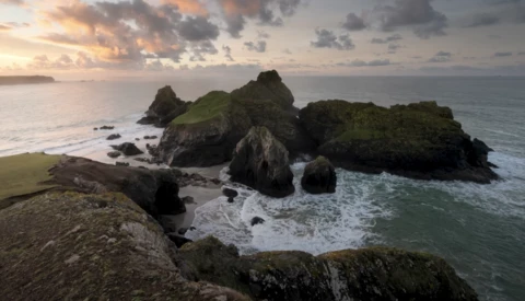 Rocky sea stacks with green vegetation rising from ocean at golden hour with dramatic sky.