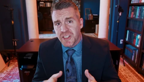 Man in business attire speaking directly to camera in a home office setting.